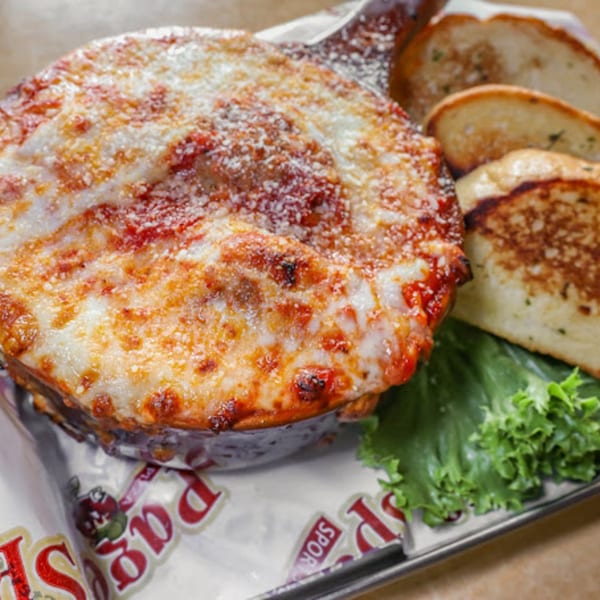 Baked pasta dish with melted cheese and red sauce, served with garlic bread and lettuce.
