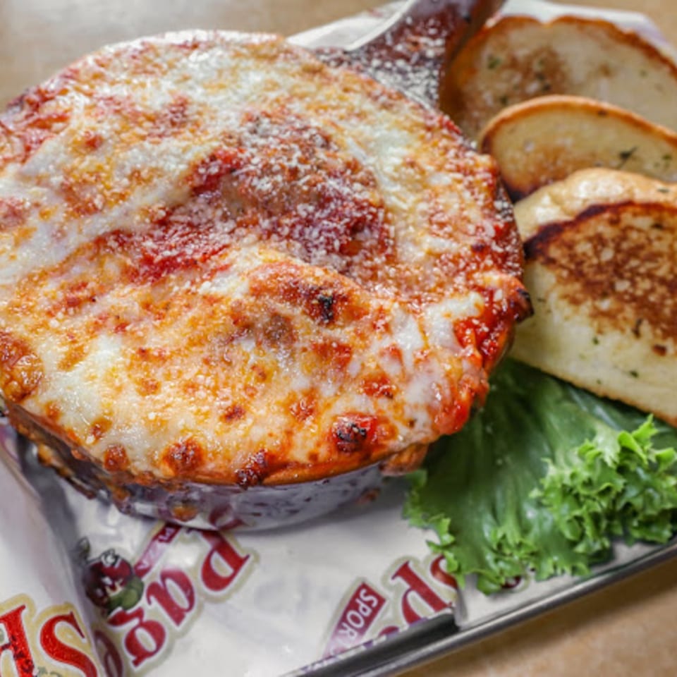 Baked pasta dish with melted cheese and red sauce, served with garlic bread and lettuce.