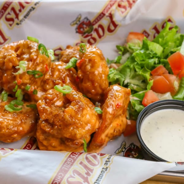 Stevie Tomato's boneless wings coated in orange sauce, garnished with green onions, served with a side salad and ranch.